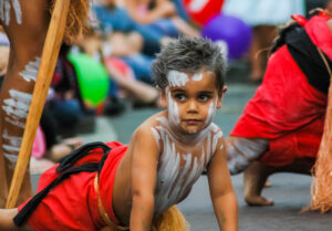 A young boy is wearing traditional dress and facepaint for NAIDOC week celebrations